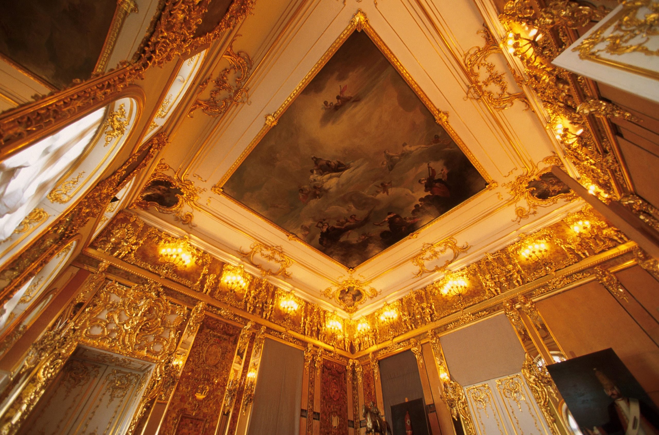 A royal room covered throughout with amber and gold, with a painting on its ceiling