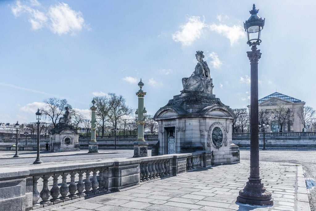 Photograph of Parisian Neo-Classical architecture and monument and several lamp posts on a sunny day.