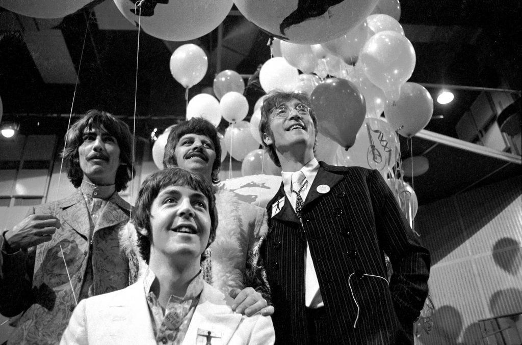 a black and white photograph of four men in black and white suits posing against a background with balloons for a celebration