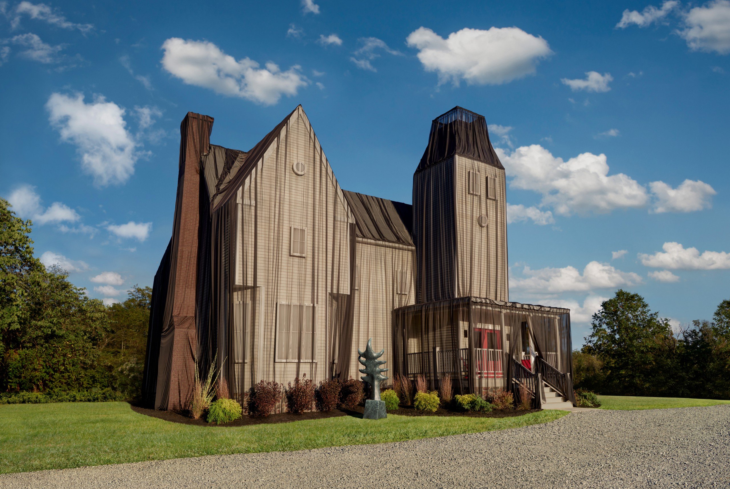 a large wooden house shrouded by a dark veil in a green field under a blue sky surrounded by trees