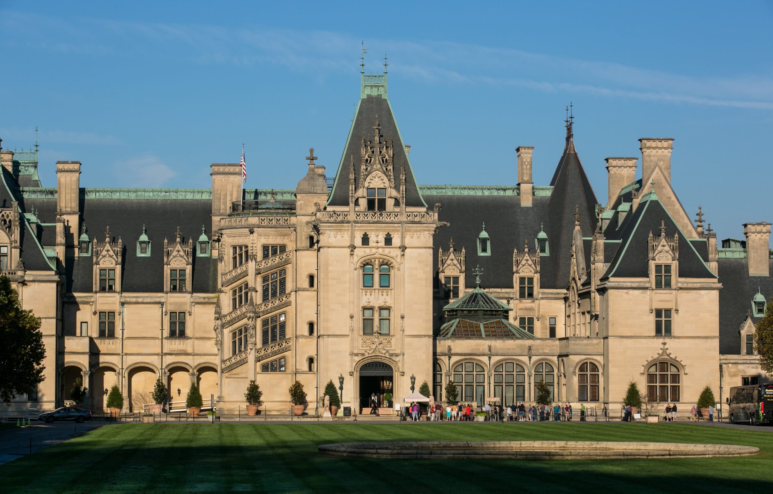 an old, large mansion with lots of windows under a blue sky in front of a lawn with people walking across