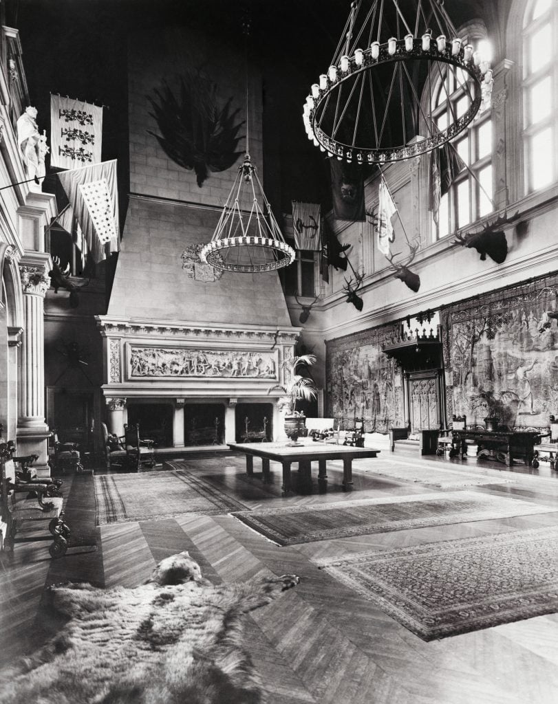 a black and white photo of a large room with a fireplace and chandeliers hanging from the ceiling