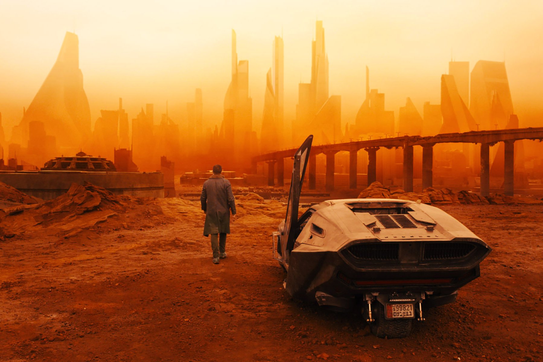 Still from the film Blade Runner 2049 showing a man walking away from a futuristic vehicle against an orange-tinted cityscape