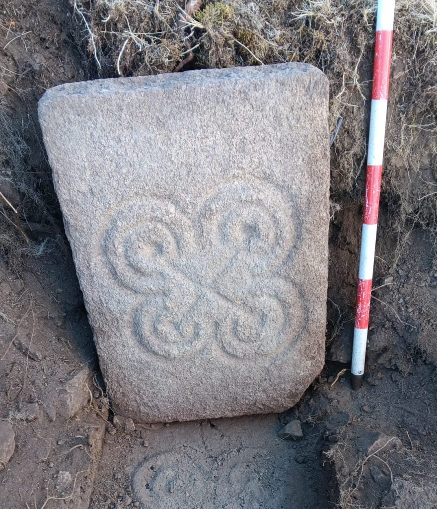 A stone slab carved with an ornate circular design sitting in a trench