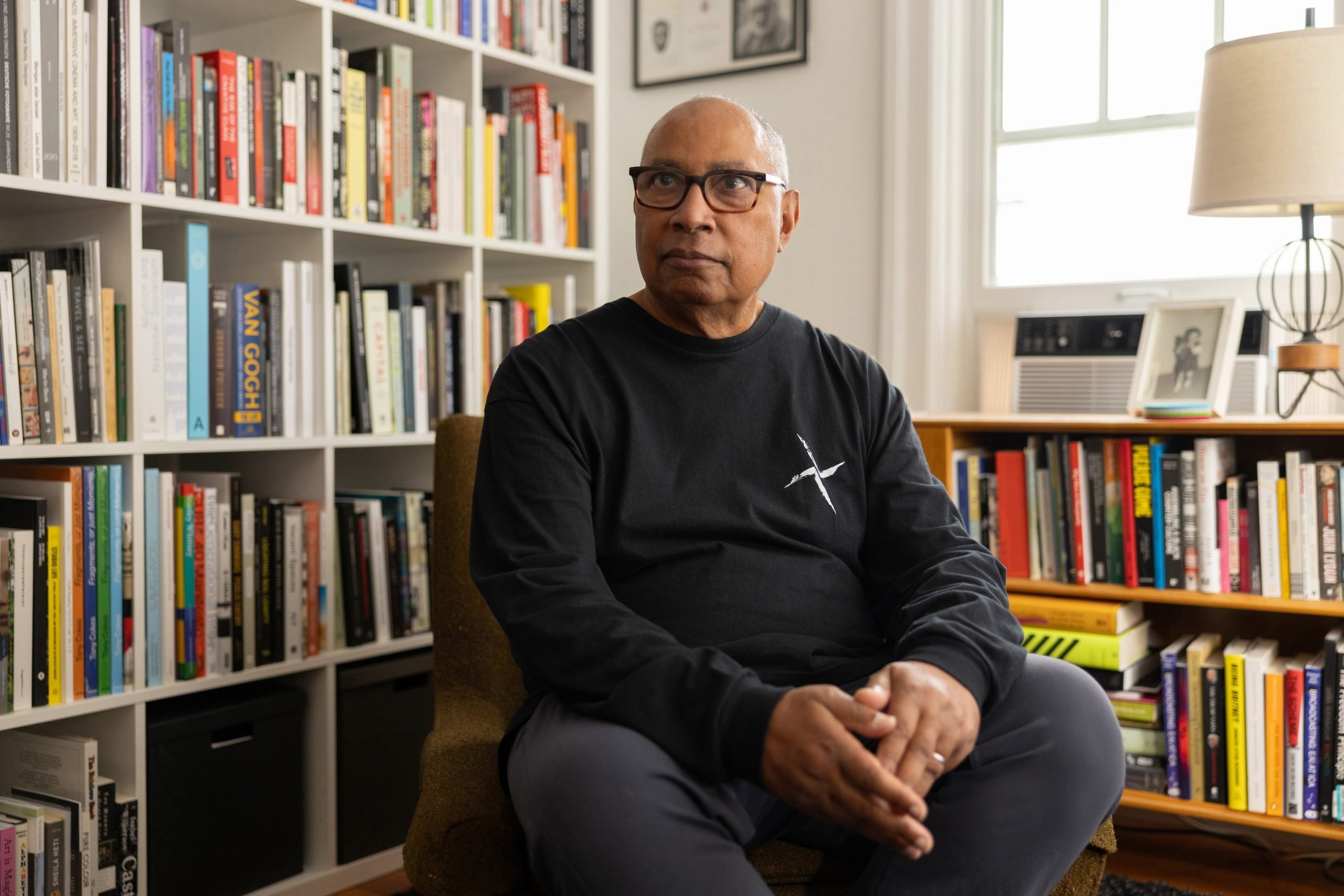 A photograph of artist Tony Cokes seated in his library