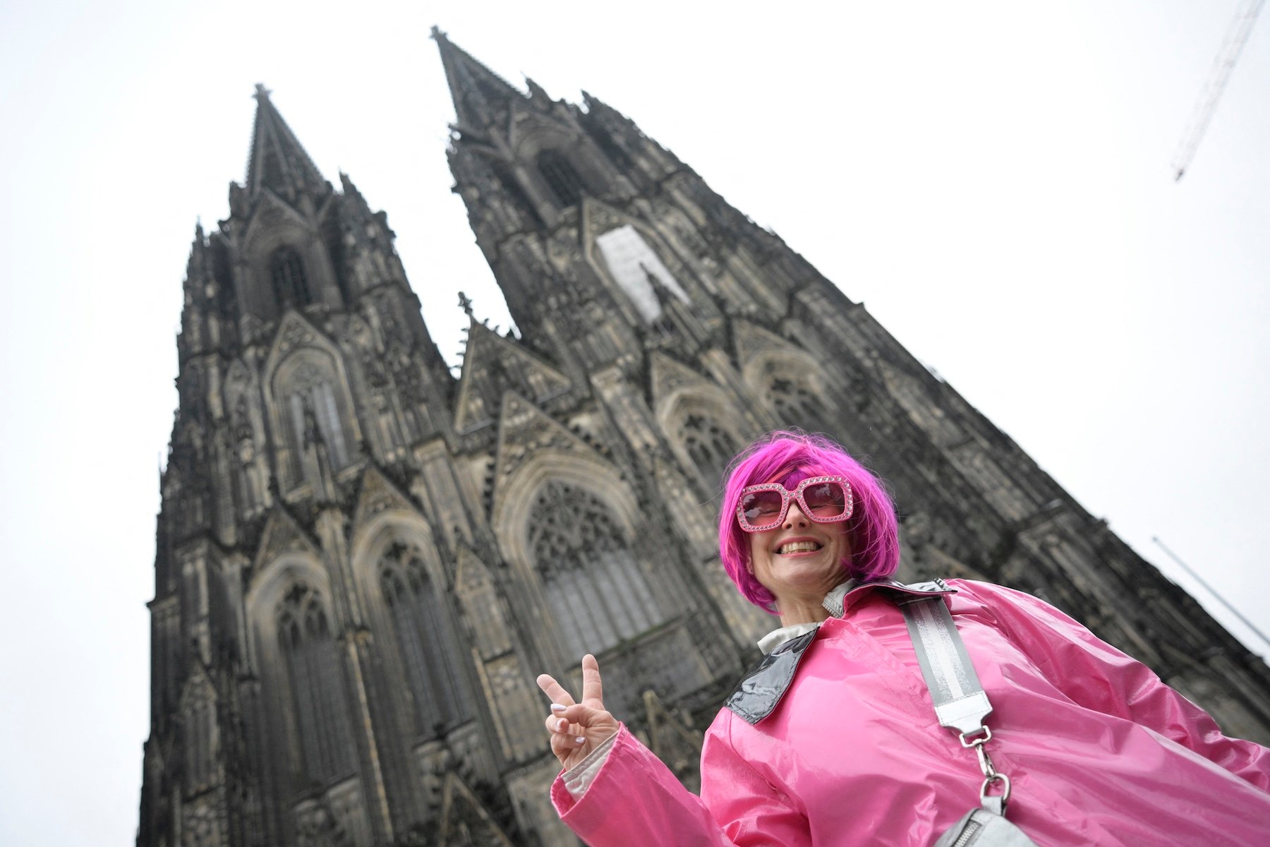 A woman with a bright pink wig poses in front of a towering Gothic cathedral