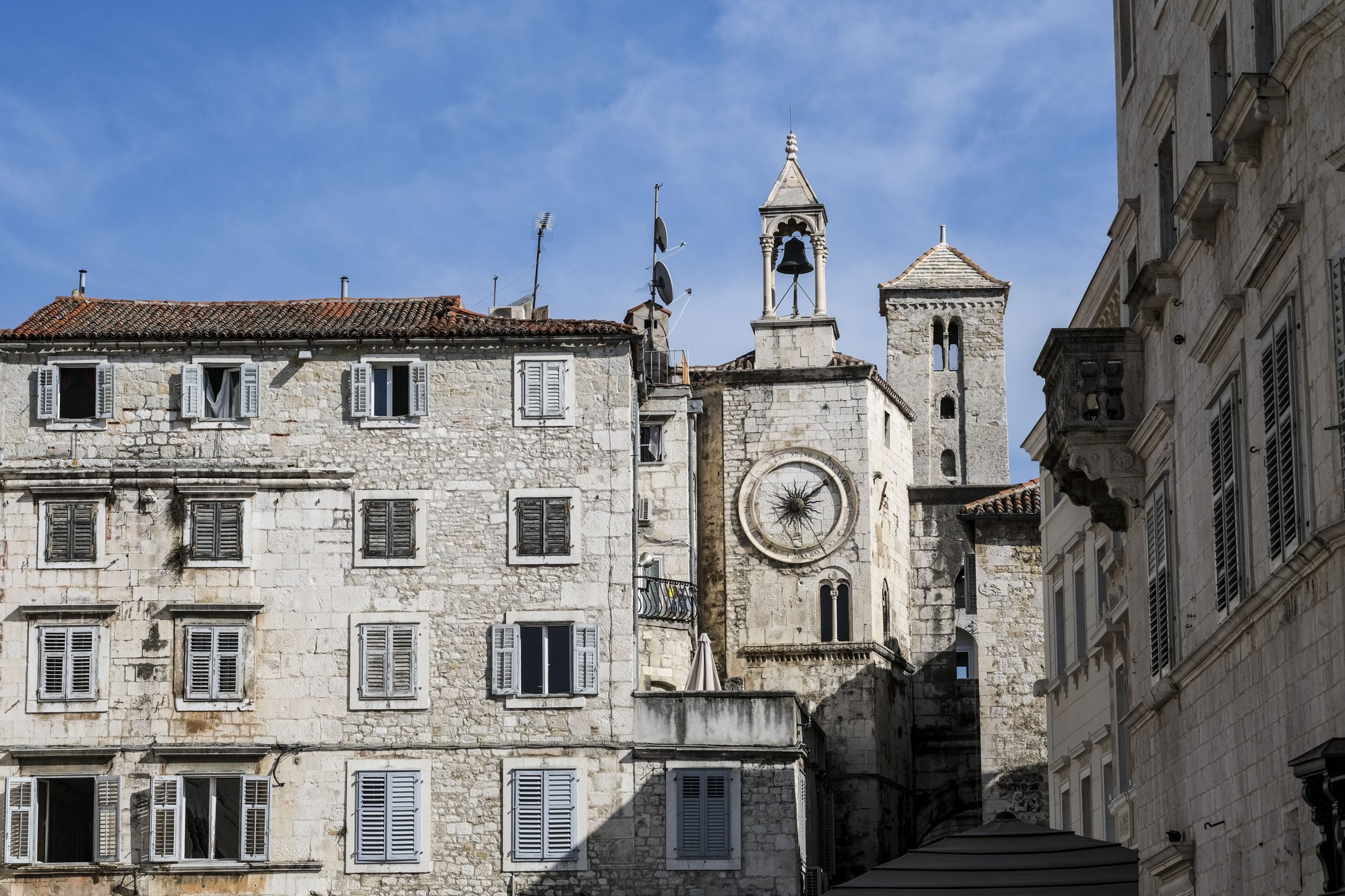 A clock tower is pictured alongside a stone building against a bright blue sky