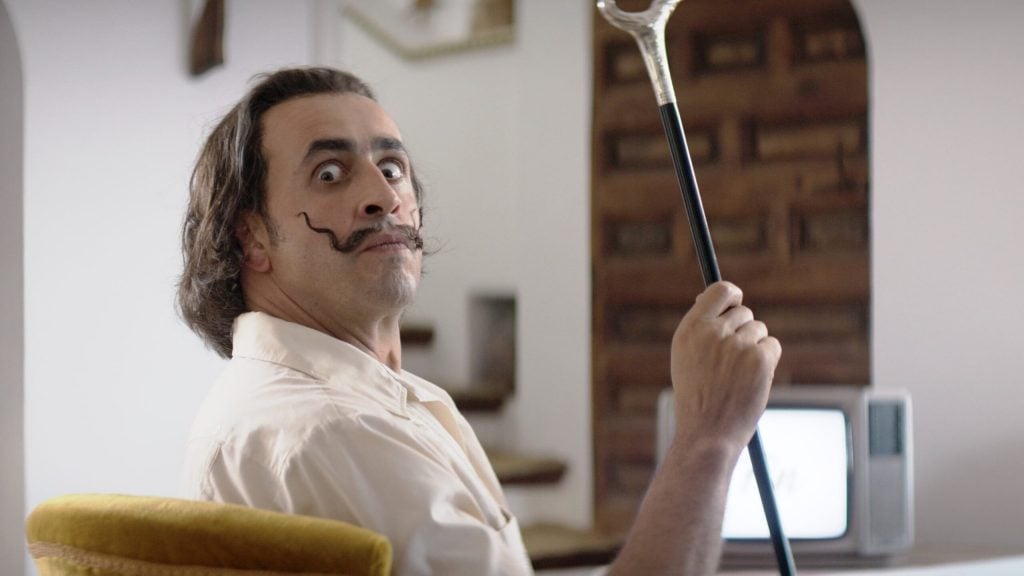 In a still from the film Daaaaaalí, a man wearing a surprised look and a wiry mustache, holds a cane up. 