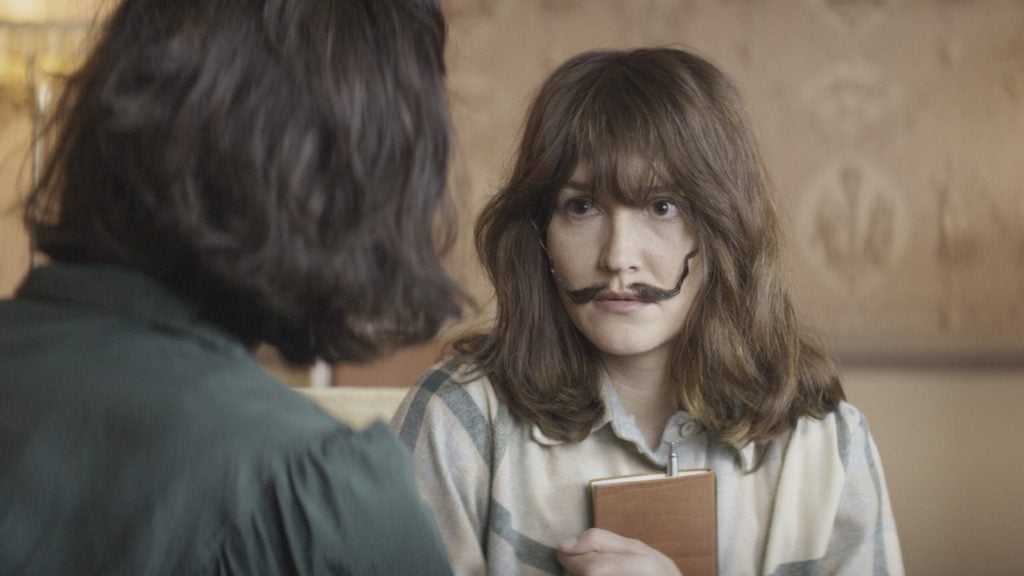 In a still from the film Daaaaaalí, a woman with a wiry mustache sits looking at a man