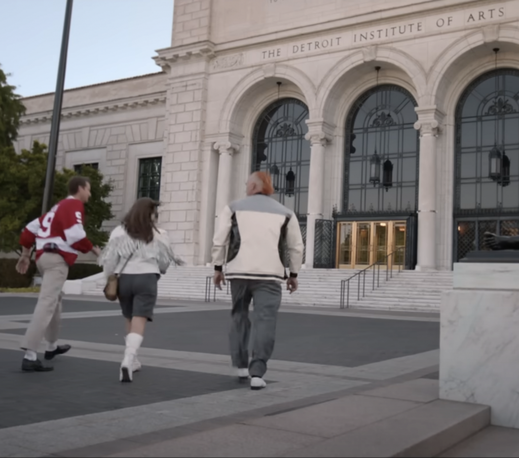 A still from "Darren McCarty's Day Off" from filming at the Detroit Institute of Arts. Three adults are seen from behind walking up to the museum entrance. 