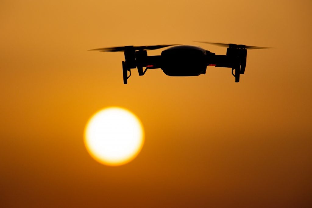 A quadcopter drone hovering during a flight in front of the sun.