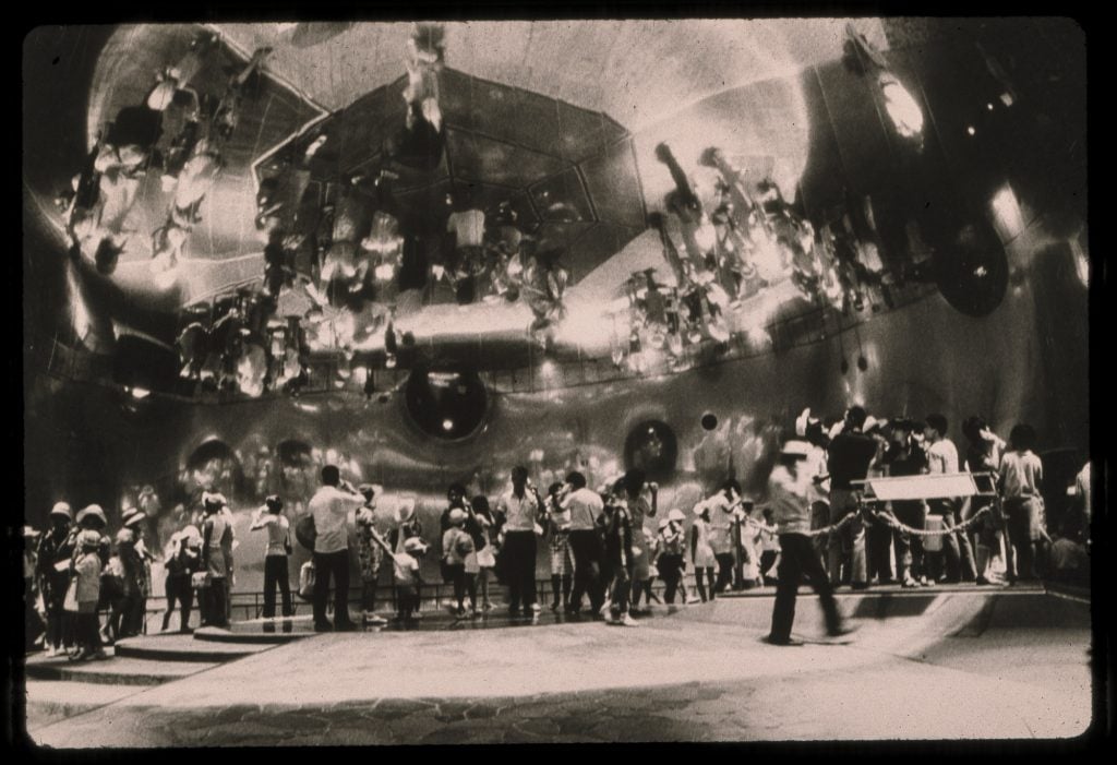 A crowd milling inside of a large mirrored dome with mirrors on the walls