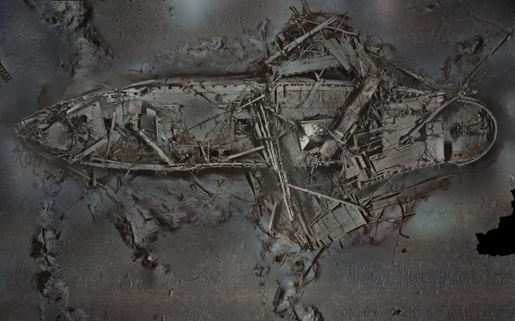 photo of a shipwreck at the bottom of the sea lying on top of a bed of rocks and sand with broken masts and oars