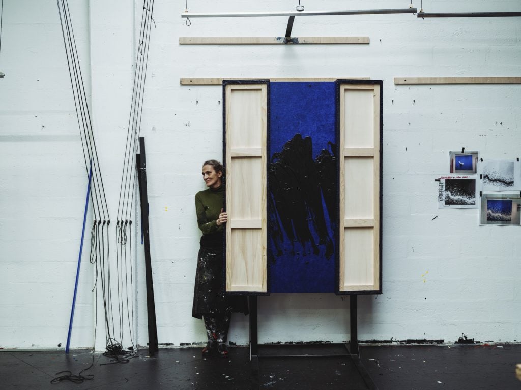 Artist Fabienne Verdier standing next to one of her large-scale abstract paintings with two panels folded inwards as part of a triptych.