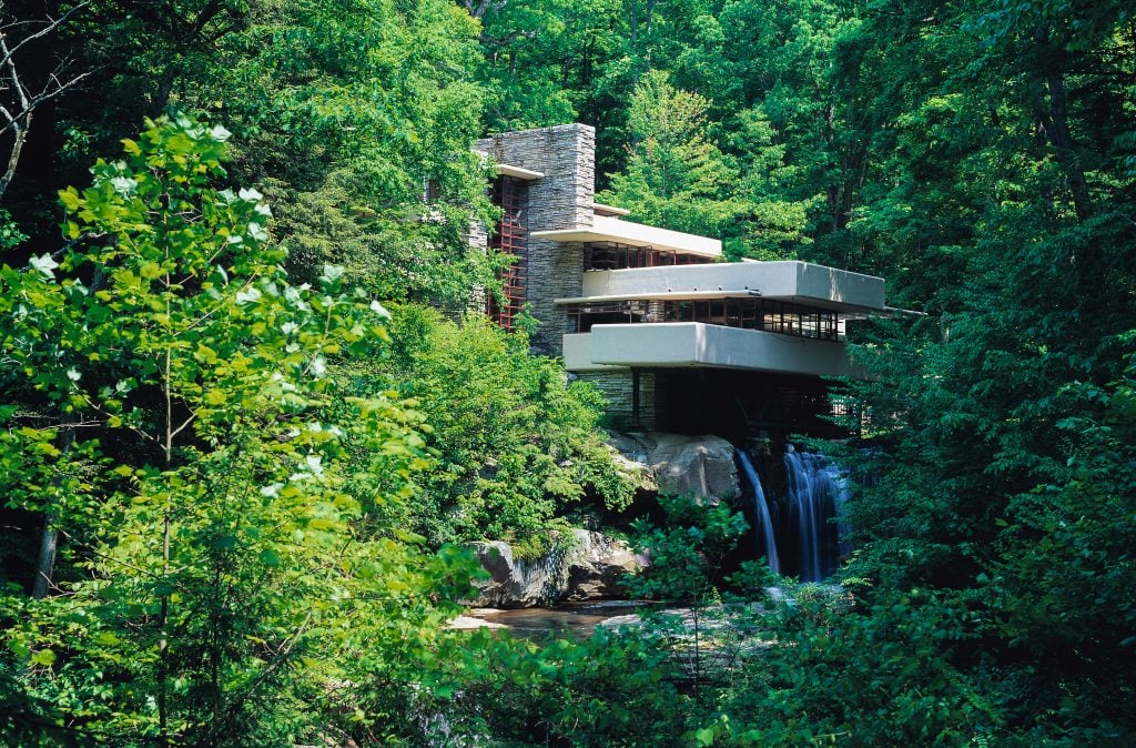 A photo showing Fallingwater, a house with a series of terraces hanging over a waterfall amid lush greenery