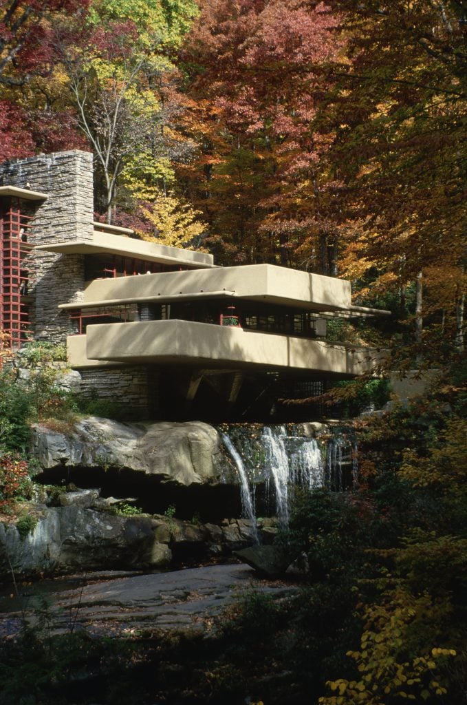 A photo showing Fallingwater, a house with a series of terraces hanging over a waterfall amid lush greenery