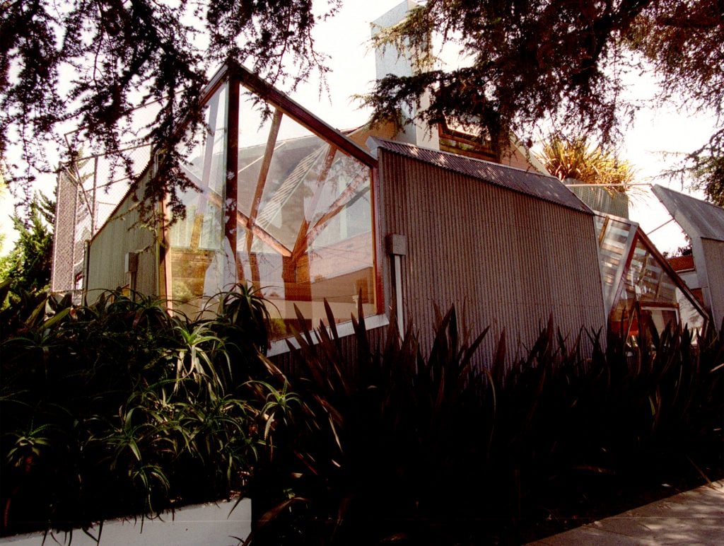 A house made of corrugated iron and glass panes jutting out at sharp angles, along a suburban street