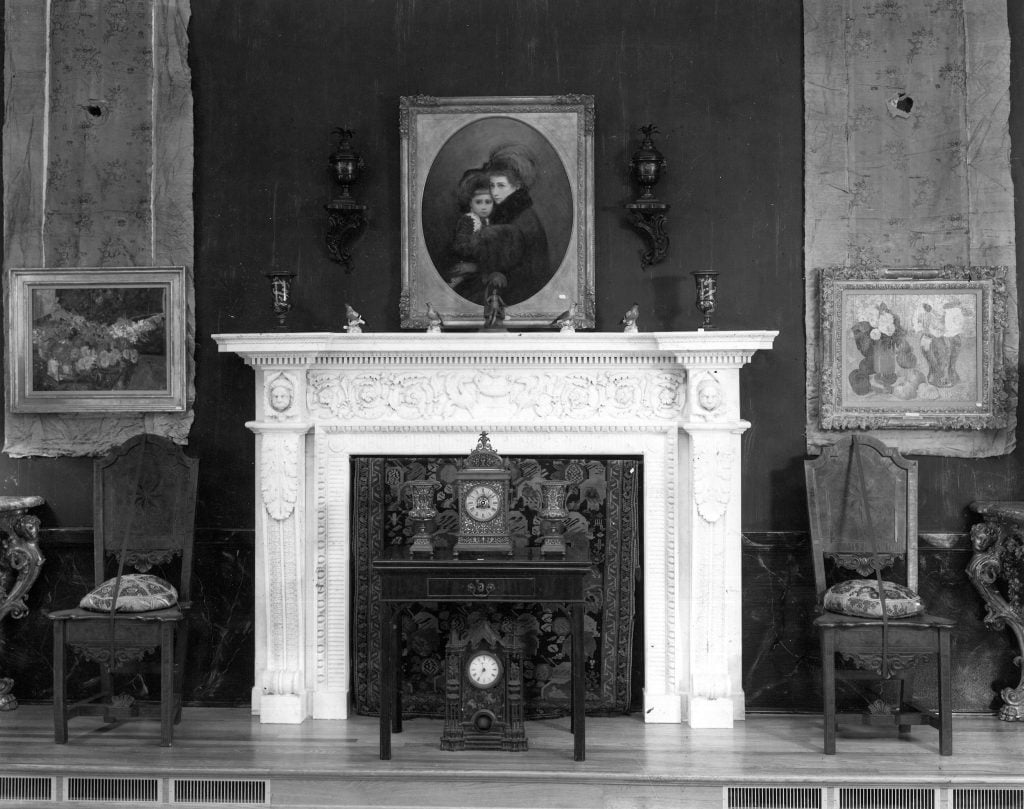 A museum display showing a large white mantle, with paintings beside and on top of it