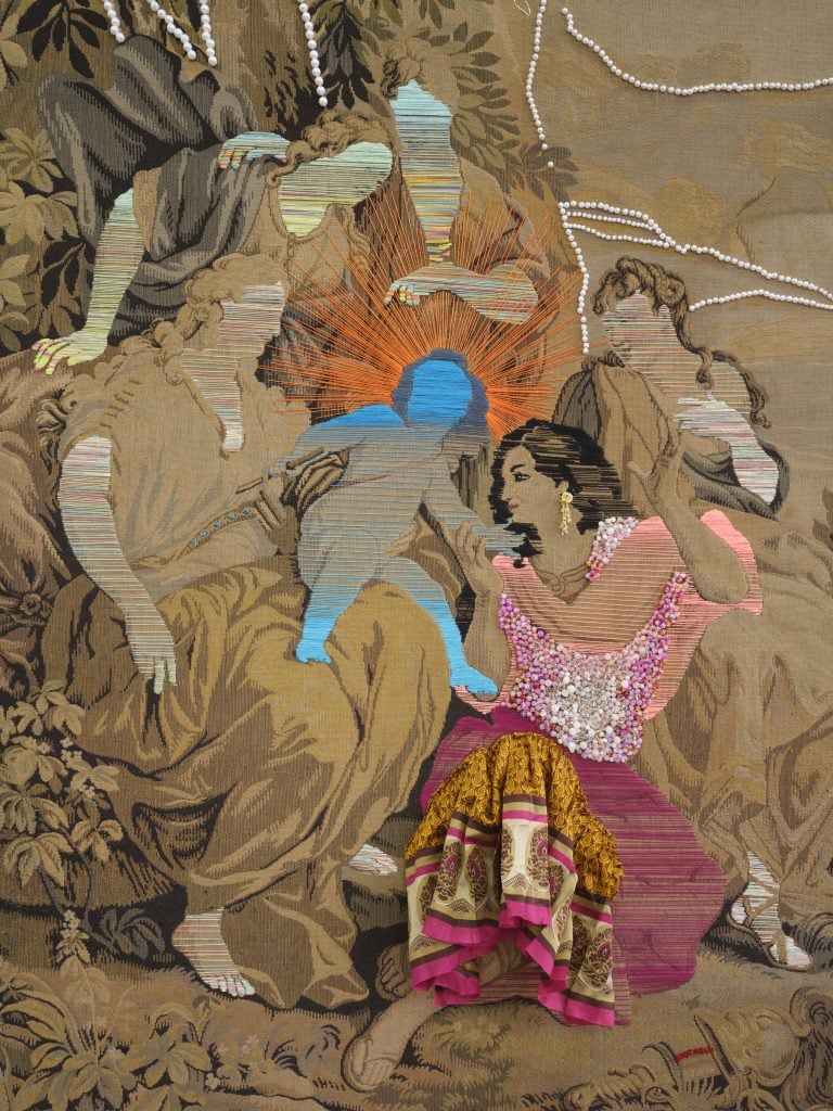 A tapestry made of antique fabric overlaid with colorful thread and brightly patterned saris. Five seated adult figures surround a baby. Their faces are covered with embroidery thread, except for one female figure who is adorned with bright fabric, and grasps the baby.