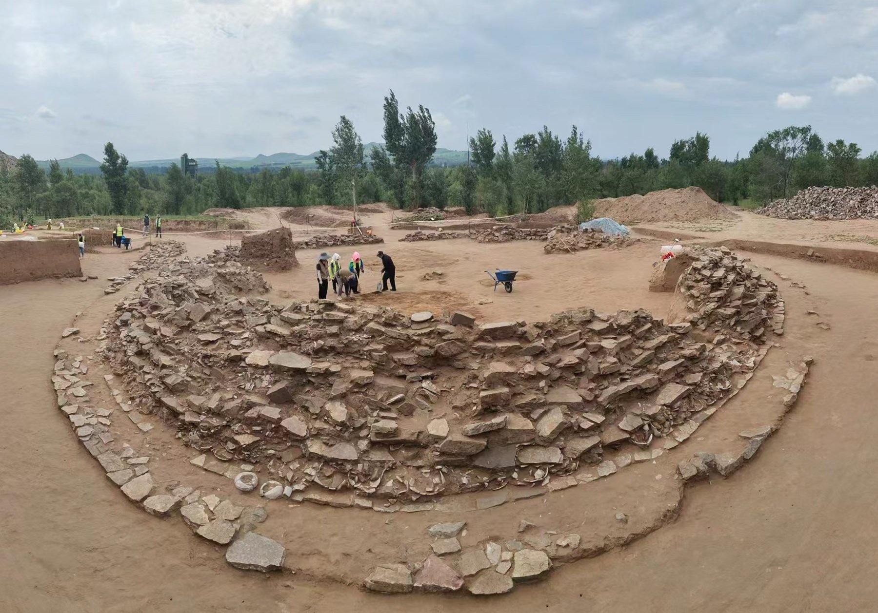 a round tomb with people working on it, there are trees in the background and sky above