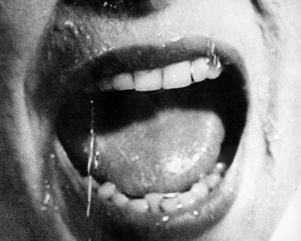 Black and white close-up of a woman's mouth screaming, with saliva dripping down her chin