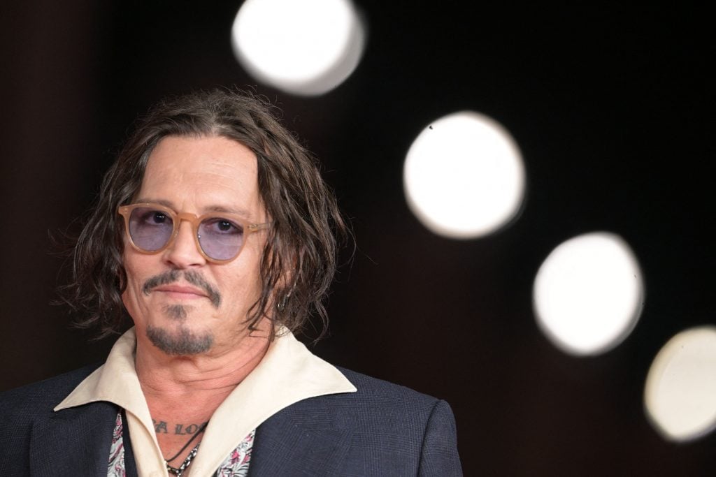 Johnny Depp in sunglasses and a suit posing against a series of white lights