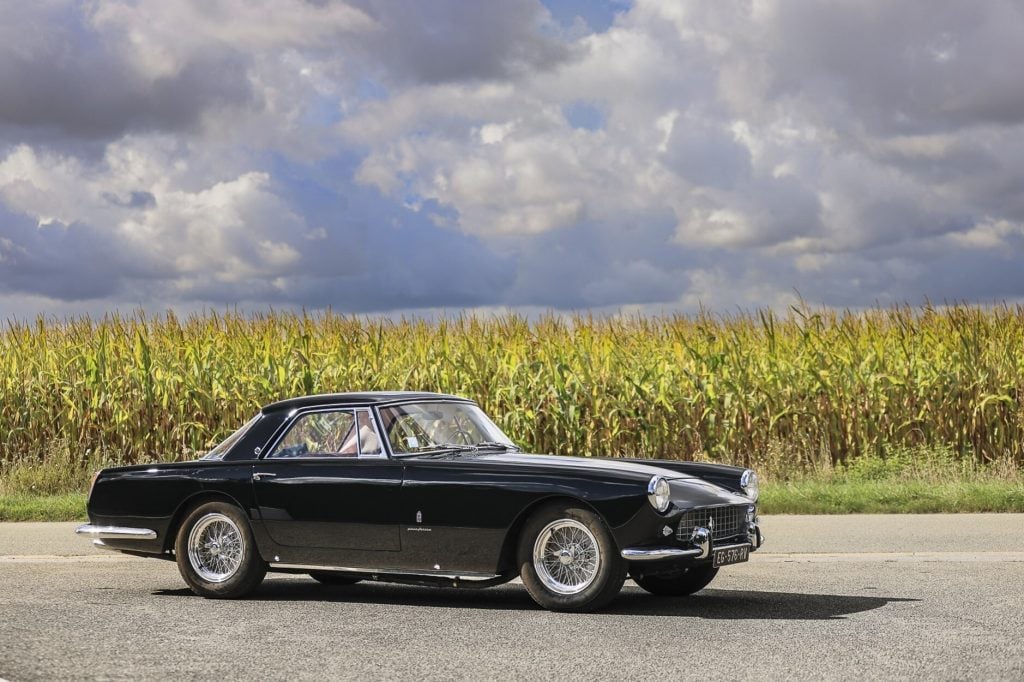 A black 1958 Ferrari parked on a road next to a field