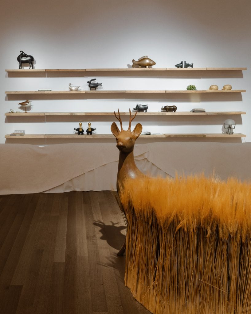 A sculpture of a deer peeking out from thigh-high wheat installed in a gallery