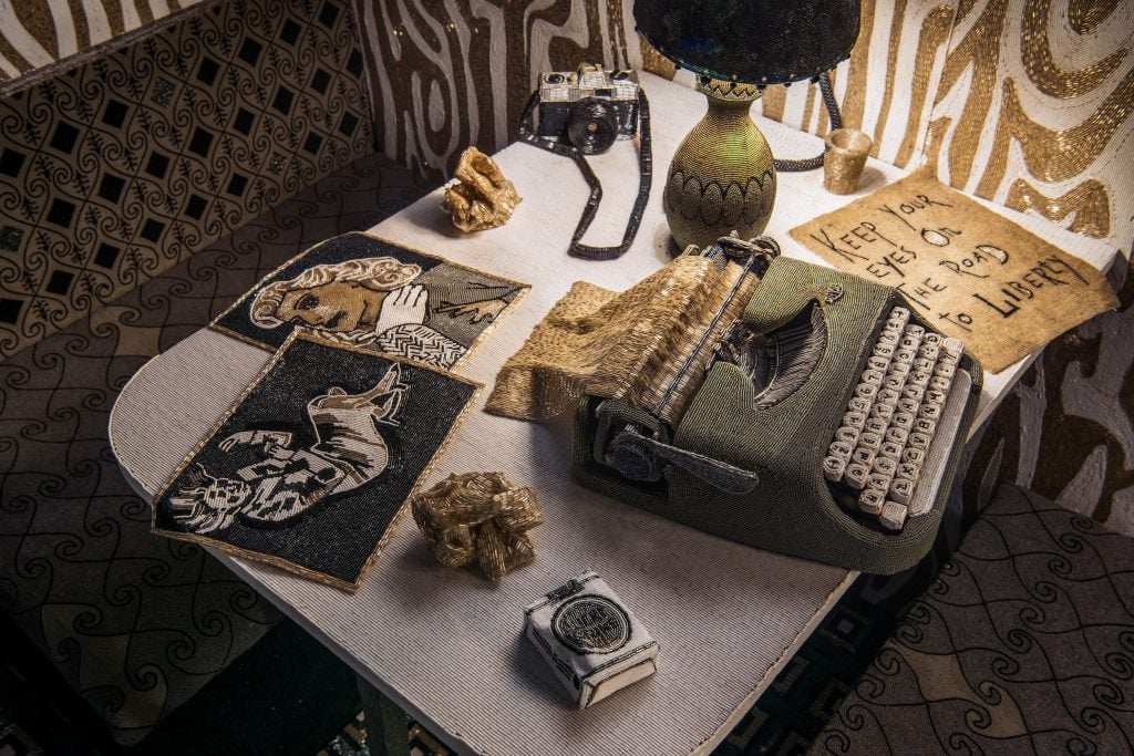 A kitchenette in the interior of a mobile trailer, every surface covered in black and white beads, a kitchenette table with a typewriter