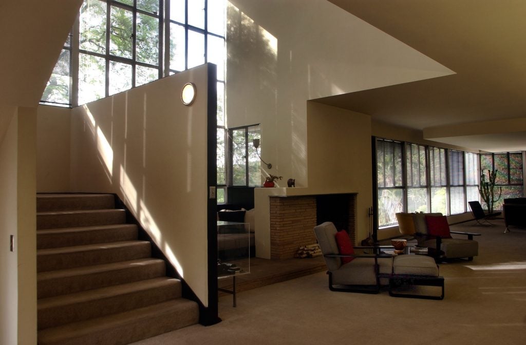 View inside Richard Neutra's Lovell House showing two long armchairs in front of a modernist fireplace and a staircase to the side