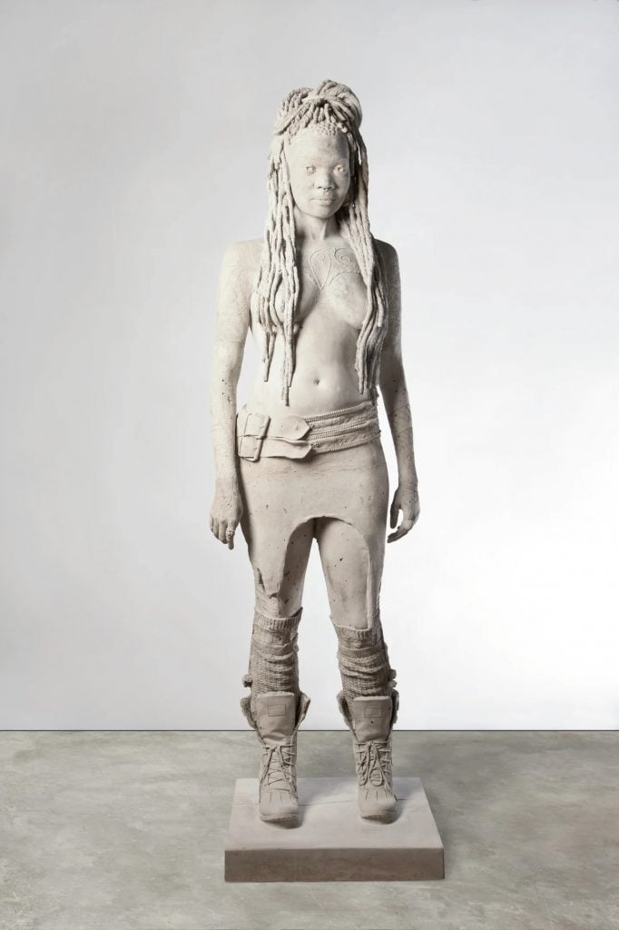 A satue in white of a woman standing wearing only pants and boots, by artist Marc Quinn and in the Autumn Sale online with Galerie Thomas.