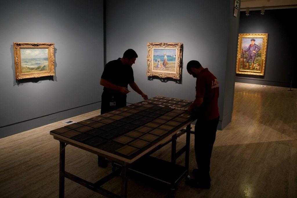 Two figures bend over a table in a museum gallery preparing small labels