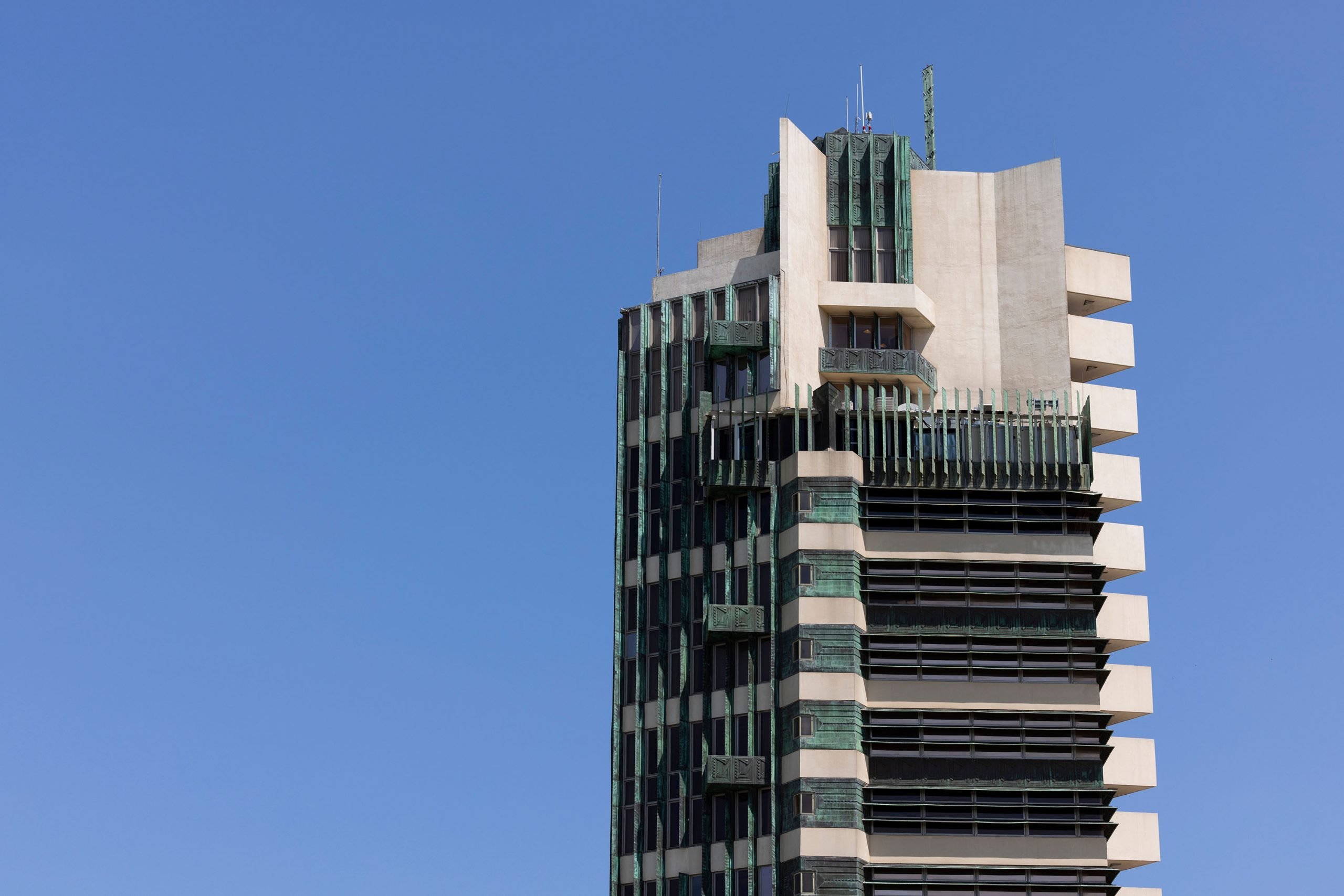 The top of a skyscraper made up of white concrete and green patina panels