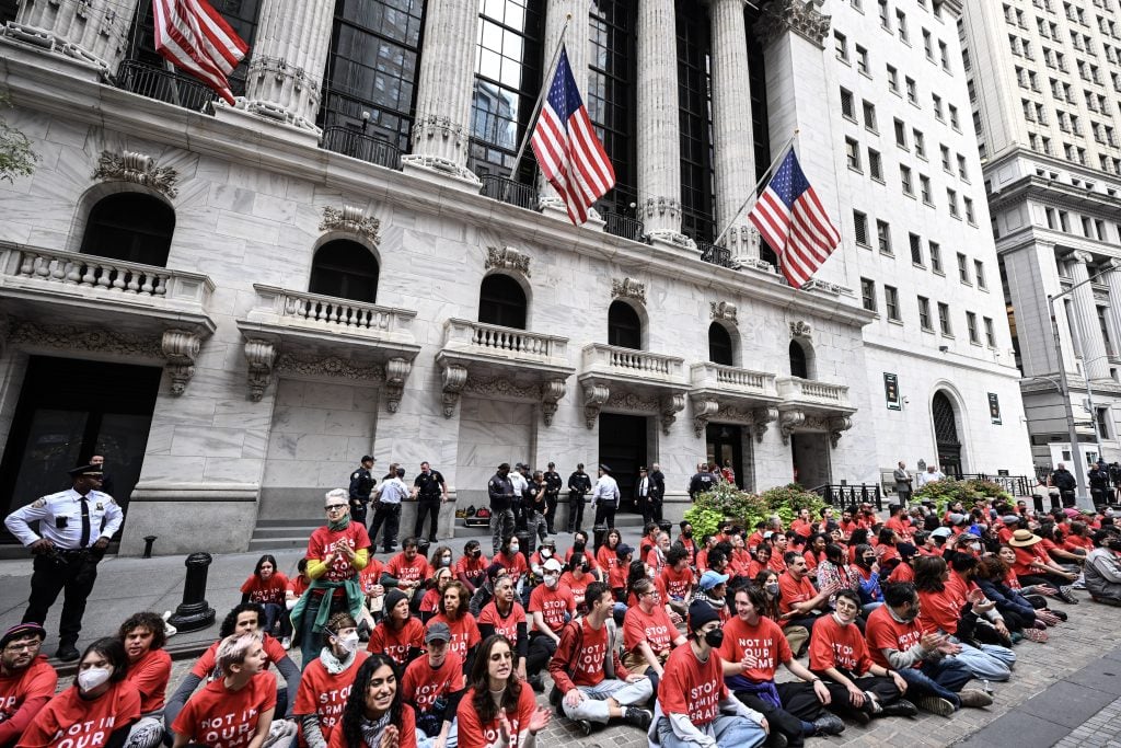 A large group of people in red t-shirts sitting on the ground outside the New York Stock Exchange