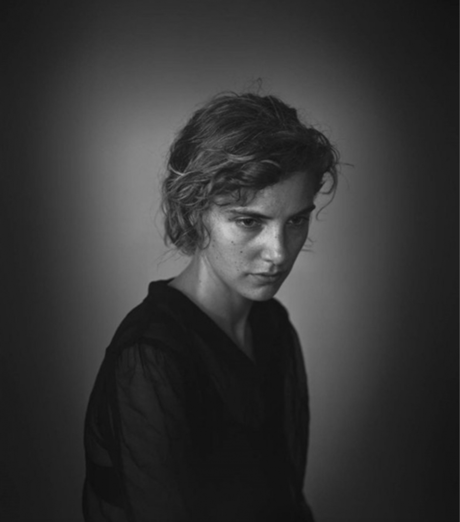 Black and white portrait of a woman wearing a black button down against a greyscale backdrop, she is lookin toward the bottom right corner of the image, by Richard Learoyd, included in Artnet's Important Photographs sale.