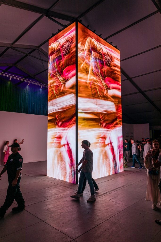 Inside the Scope Art Show 2023 with a tower of screens with abstract red lights and the outlines of people walking by.