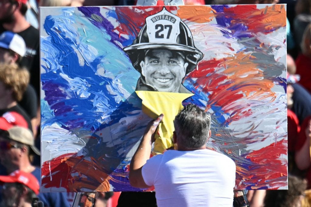 an artist unveils a portrait of a fireman against a red white and blue background