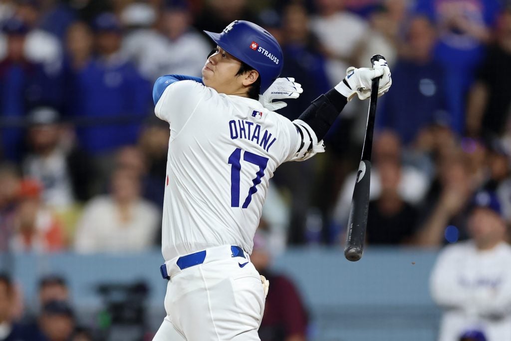 a young man with black hair in a white costume holding a baseball bat after hitting a baseball in an arena