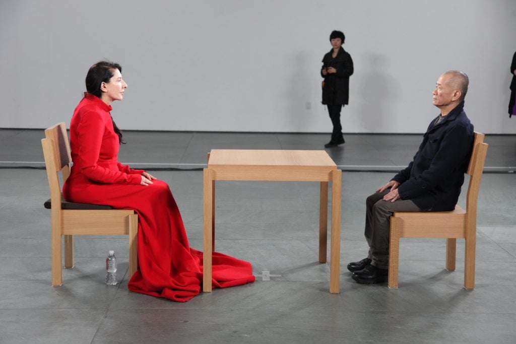 A woman in a red dress sits across the table from a Taiwanese man and they look into each other's eyes