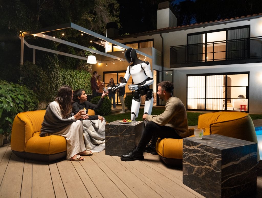 A man and two women sitting on a patio while being served by a robot