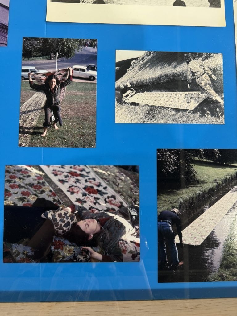 A display case from "Tina Girouard: Sign-In" featuring photographs of Tina Girouard's performance Camoplage (1977) at Documenta 6, in Kassel, Germany, washing her Solomon's Lot silk fabrics in the Fulda River. 