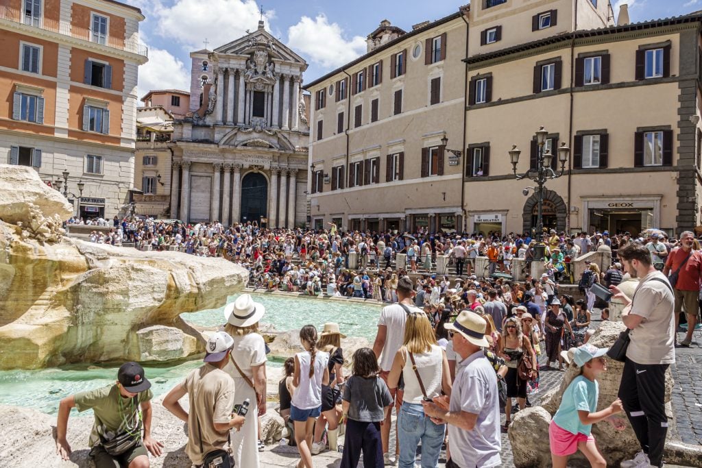 A large group of tourists surrounding the Trevi Fountain in Rome