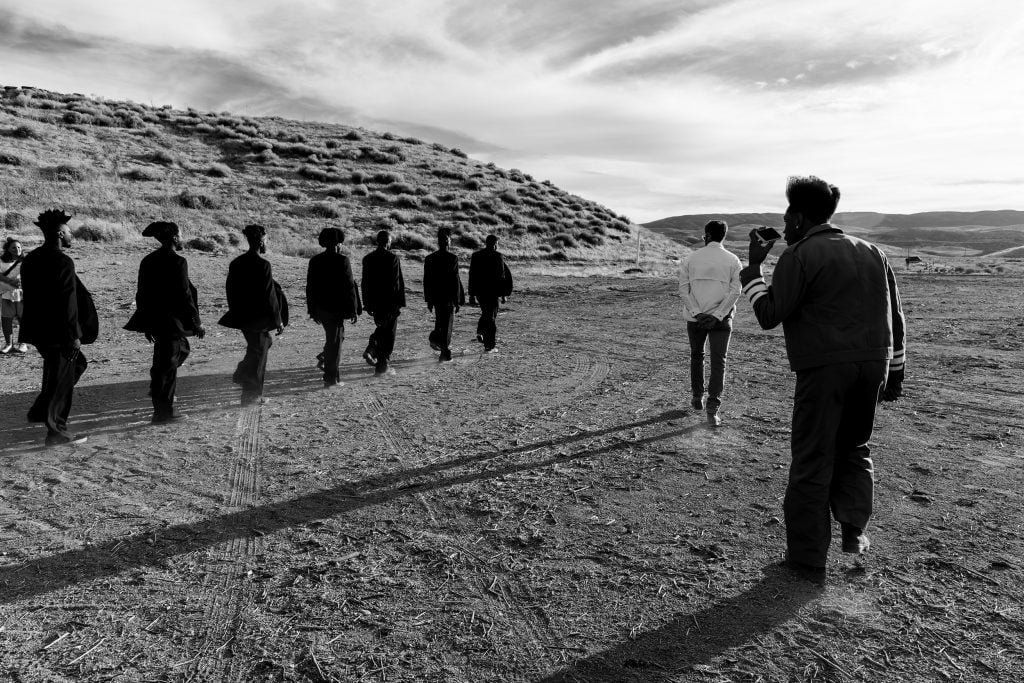 A man directing a group of people on a desert-like landscape