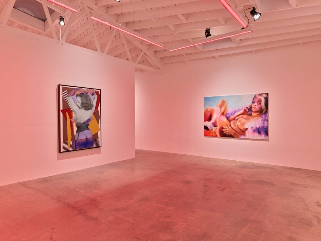 a pink-hued gallery room with two mixed media artworks on the walls depicting women in various positions