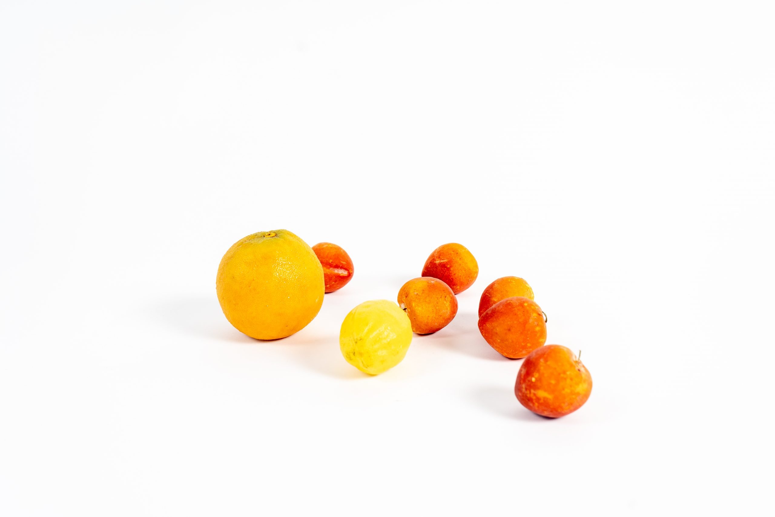 Fake apples, as well as an orange and lemon, photographed on a white backdrop.