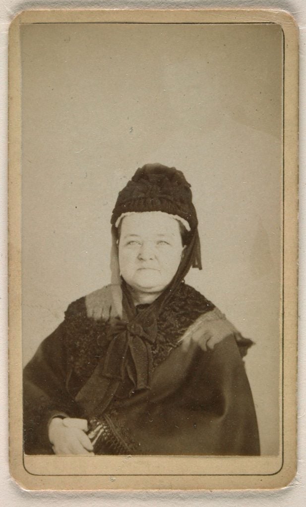 Double exposure photo of Mary Todd Lincoln posing in a black cape and bonnet, with a white figure of Abraham Lincoln behind her