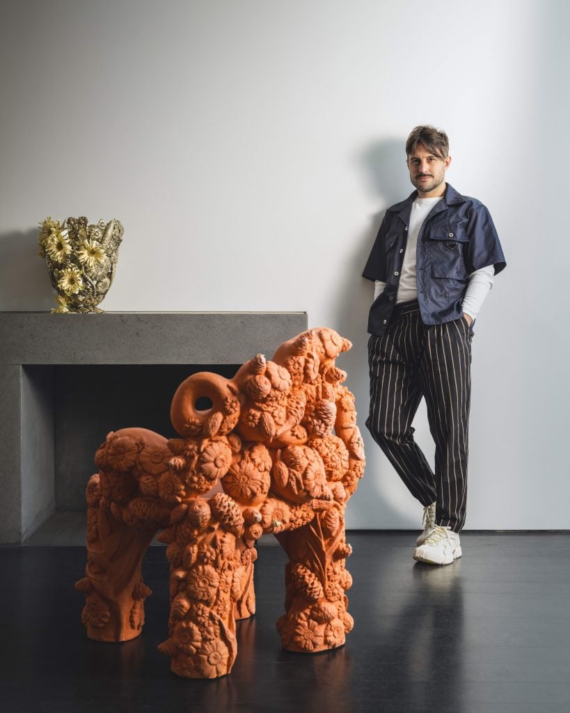 a man stands next to a high design chair and vessel atop a fireplace