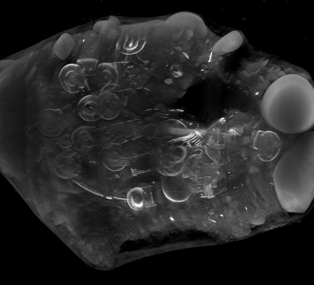 A CT scan image of the Peebles Hoard before excavation, displaying numerous overlapping circular and intricate metallic shapes embedded within the block. 