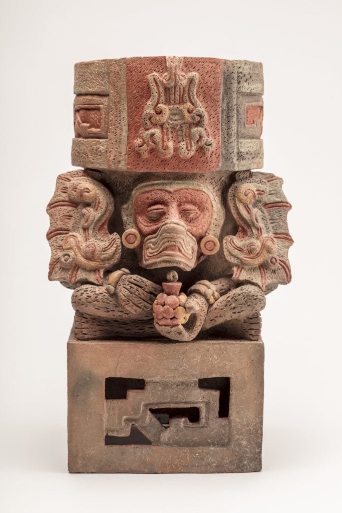 totem pole-shaped statue with several round faces poking out between two blocks stacked on top of one another