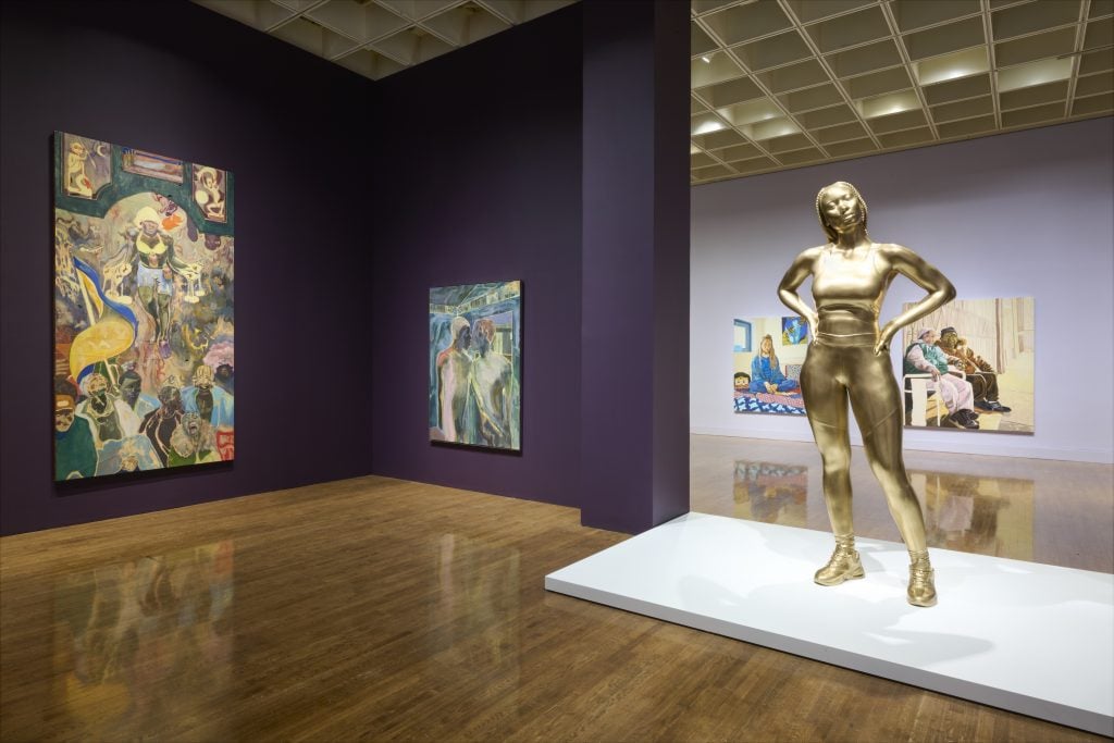 view of an exhibition feturing a gold statue and paintings in the background